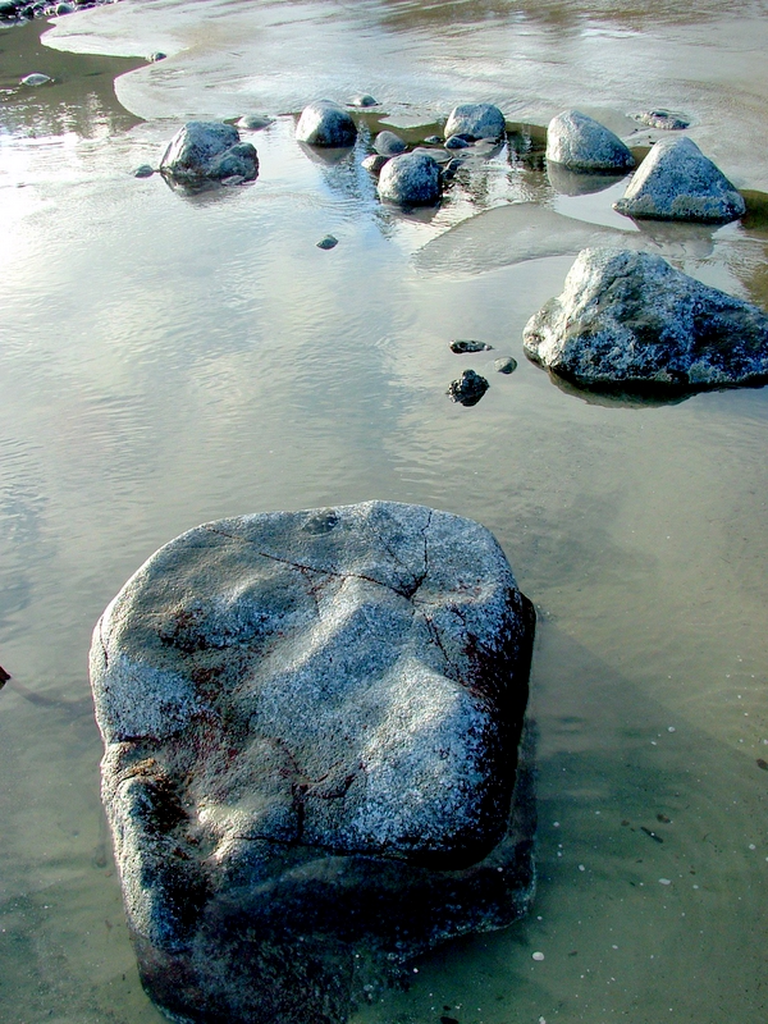 A rock in the water at the beach.