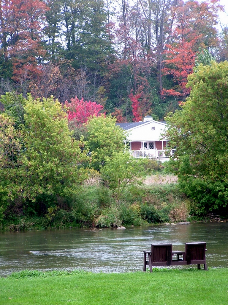 Two chairs overlook a river with a house in the background.
