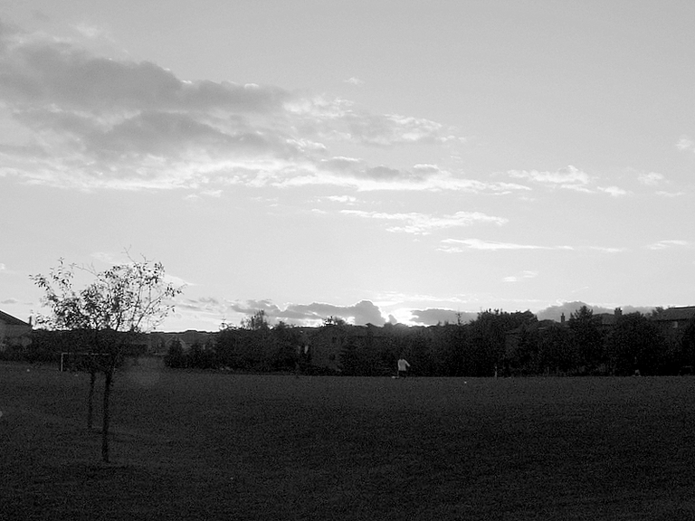 A bad black and white Sunset is the scene behind some young fellows playing soccer.
